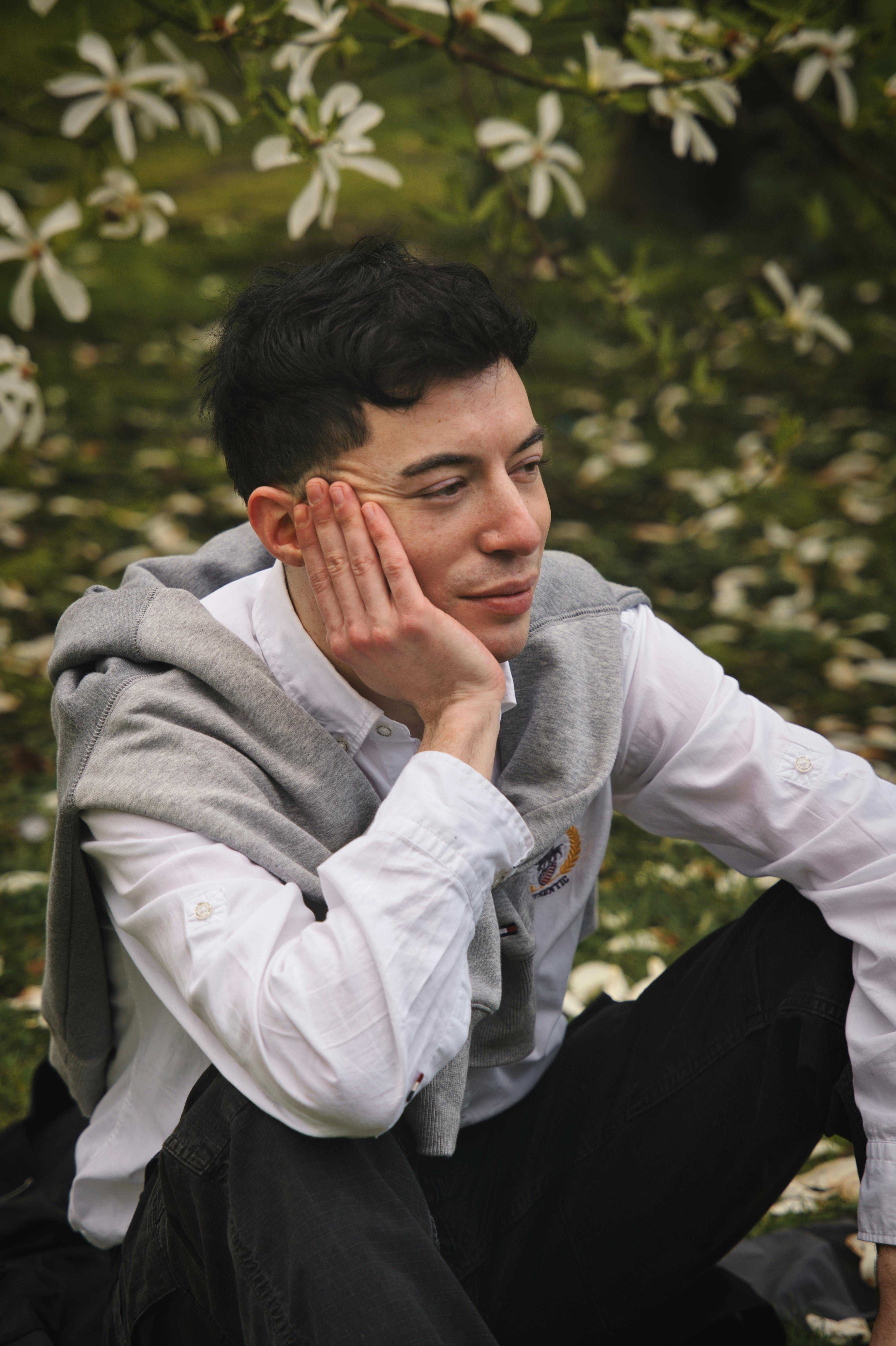 A man with short black hair pensively sits among blooming flowers in a Bremen garden.