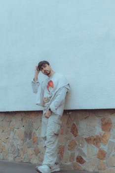 Stylish man in urban fashion leaning against a textured wall, embodying modern street style.