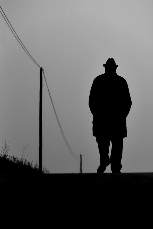 A man in a hat and coat walks down a road