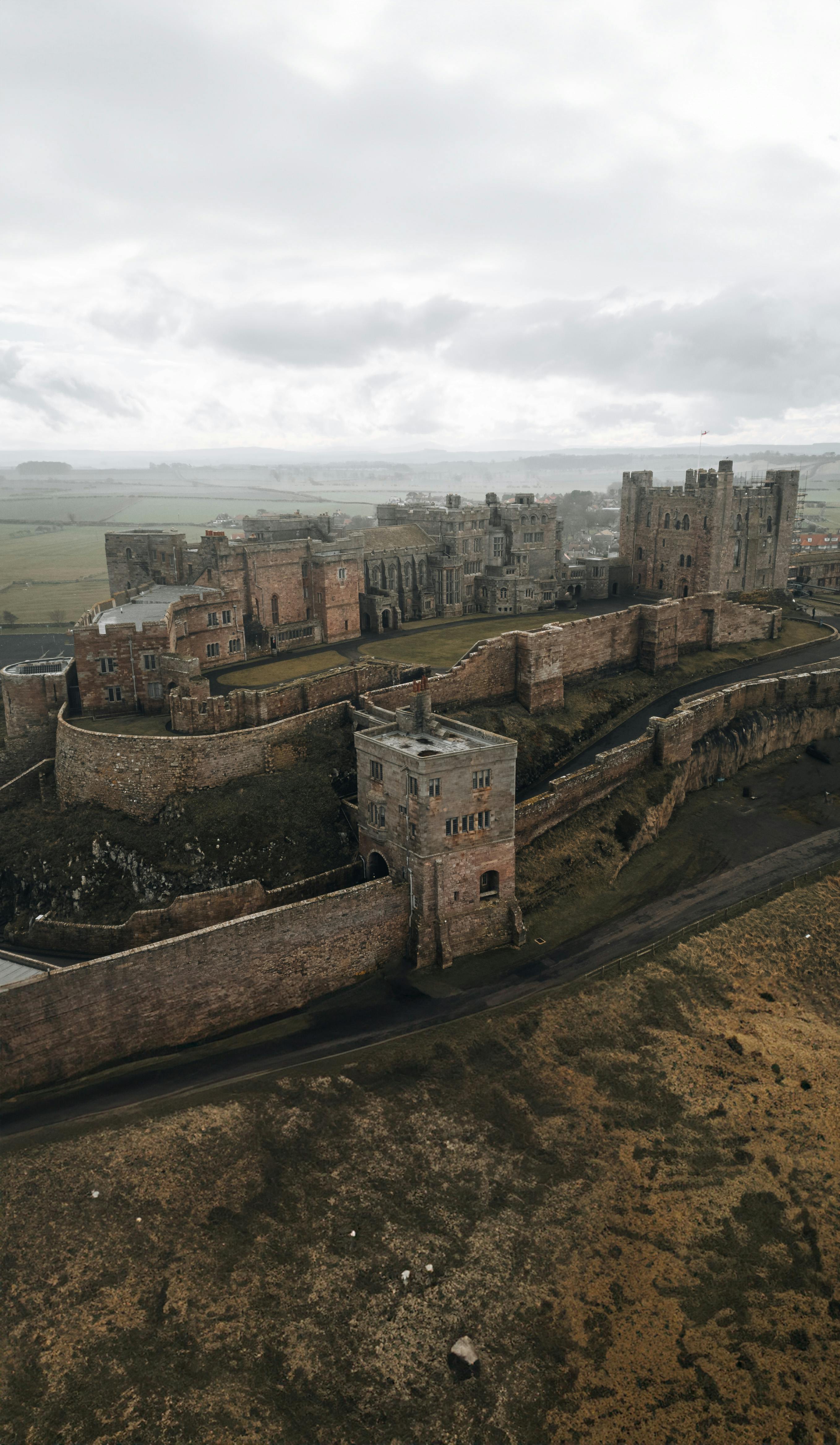 Explore the medieval charm of Bamburgh Castle in Northumberland, captured from above during a cloudy day.