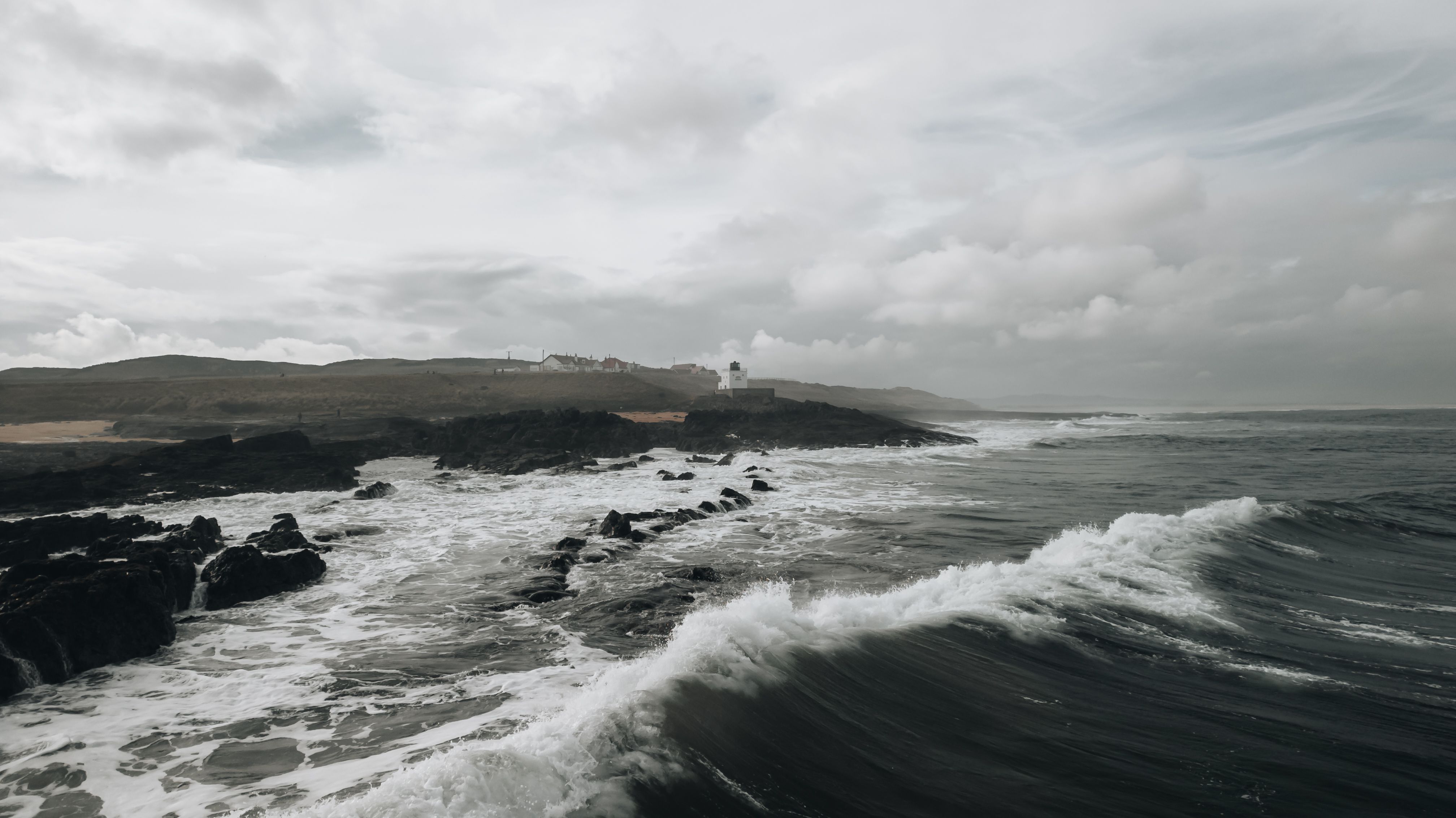 A scenic view of waves crashing against the rocky Northumberland coast with a distant lighthouse.