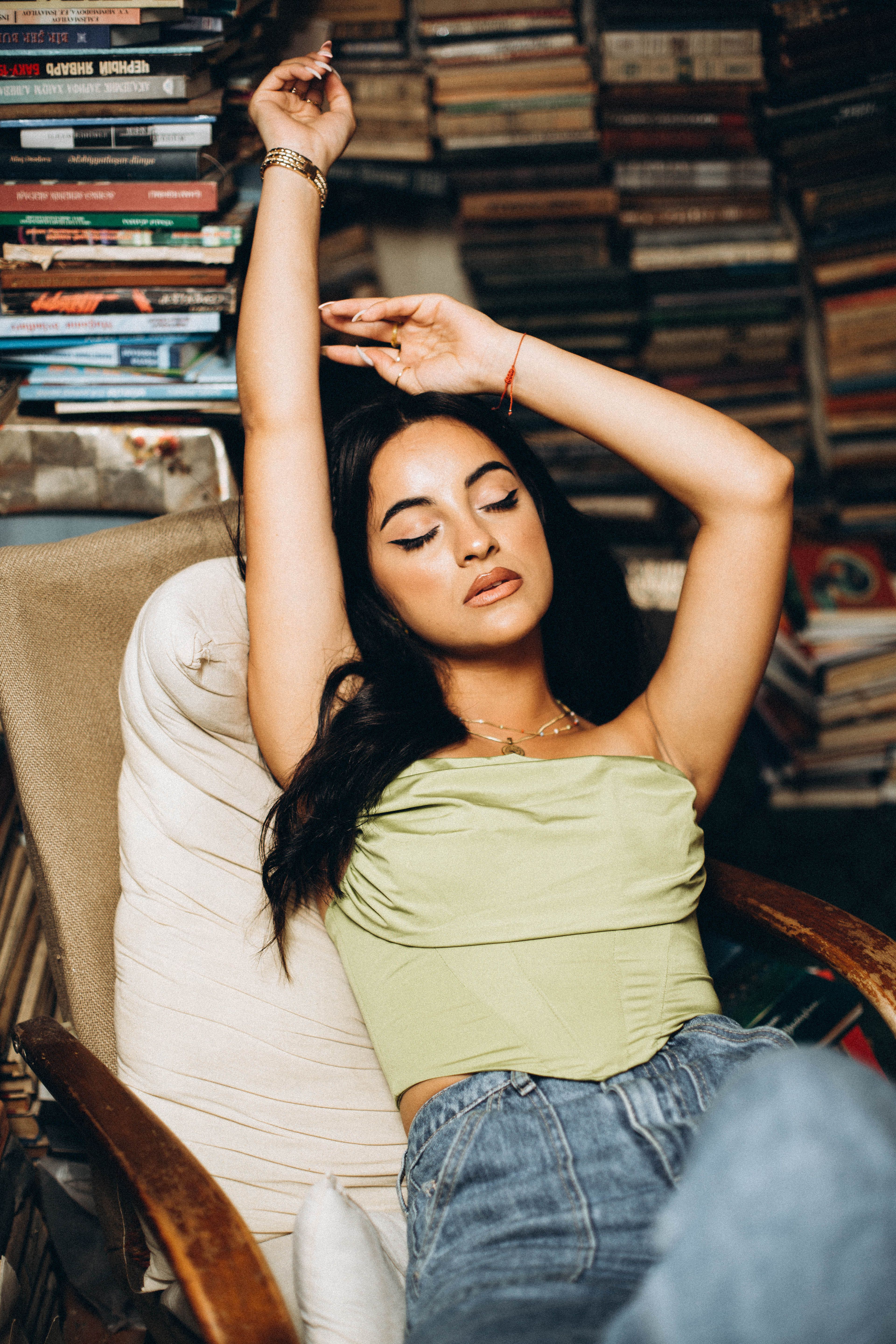 A relaxed woman with closed eyes stretches in a cozy chair surrounded by books.