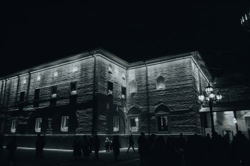 Free Nighttime view of a lit historic building with pedestrians, emphasizing its architectural features. Stock Photo