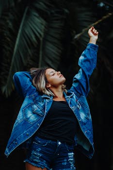 一位年轻女子身着自由的牛仔装，在绿叶背景的户外拥抱自然