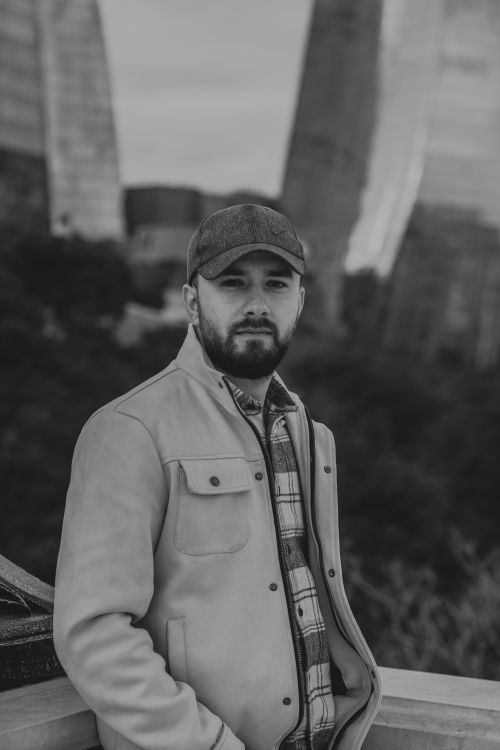 Free Stylish black and white portrait of a bearded man, wearing a cap, set against a cityscape backdrop. Stock Photo