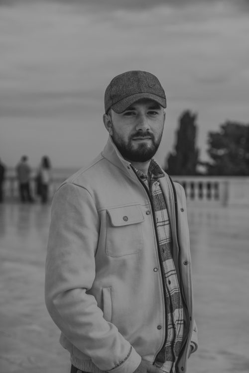 Free Portrait of a man in a cap and jacket at a seaside location, exuding calm confidence. Stock Photo