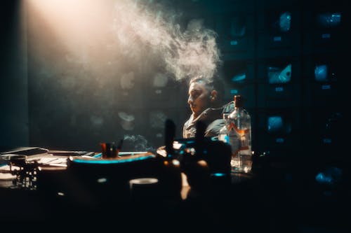 A man smoking in a dark room with a dj