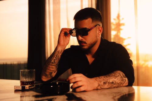 Free A man with tattoos sitting at a table with a glass of wine Stock Photo