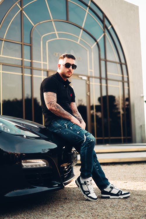 A man sitting on a black car with sunglasses