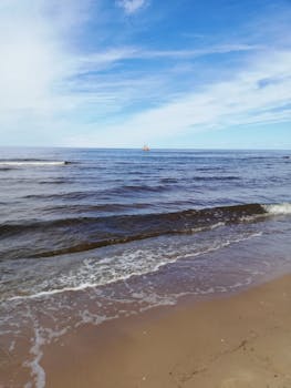 A tranquil beach scene featuring gentle waves under a bright blue sky, perfect for relaxation.
