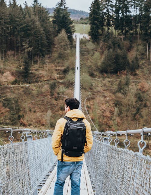 A man with a backpack walks across a suspension bridge