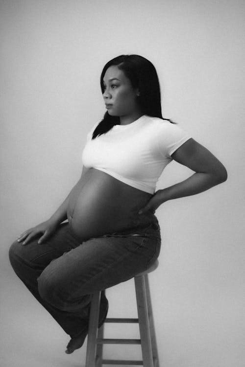 A pregnant woman sitting on a stool in black and white