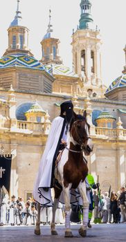 Horse rider in traditional attire at a cultural parade in Zaragoza, Spain with iconic basilica backdrop.