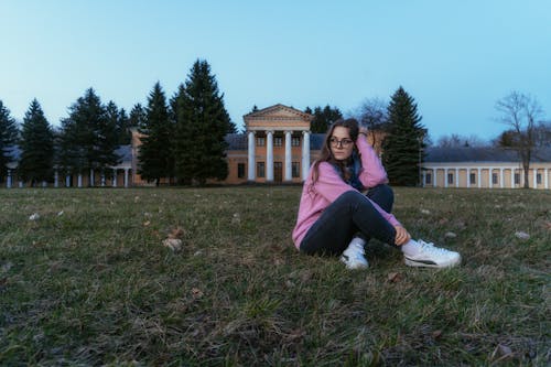 A girl sitting on the grass in front of a large building
