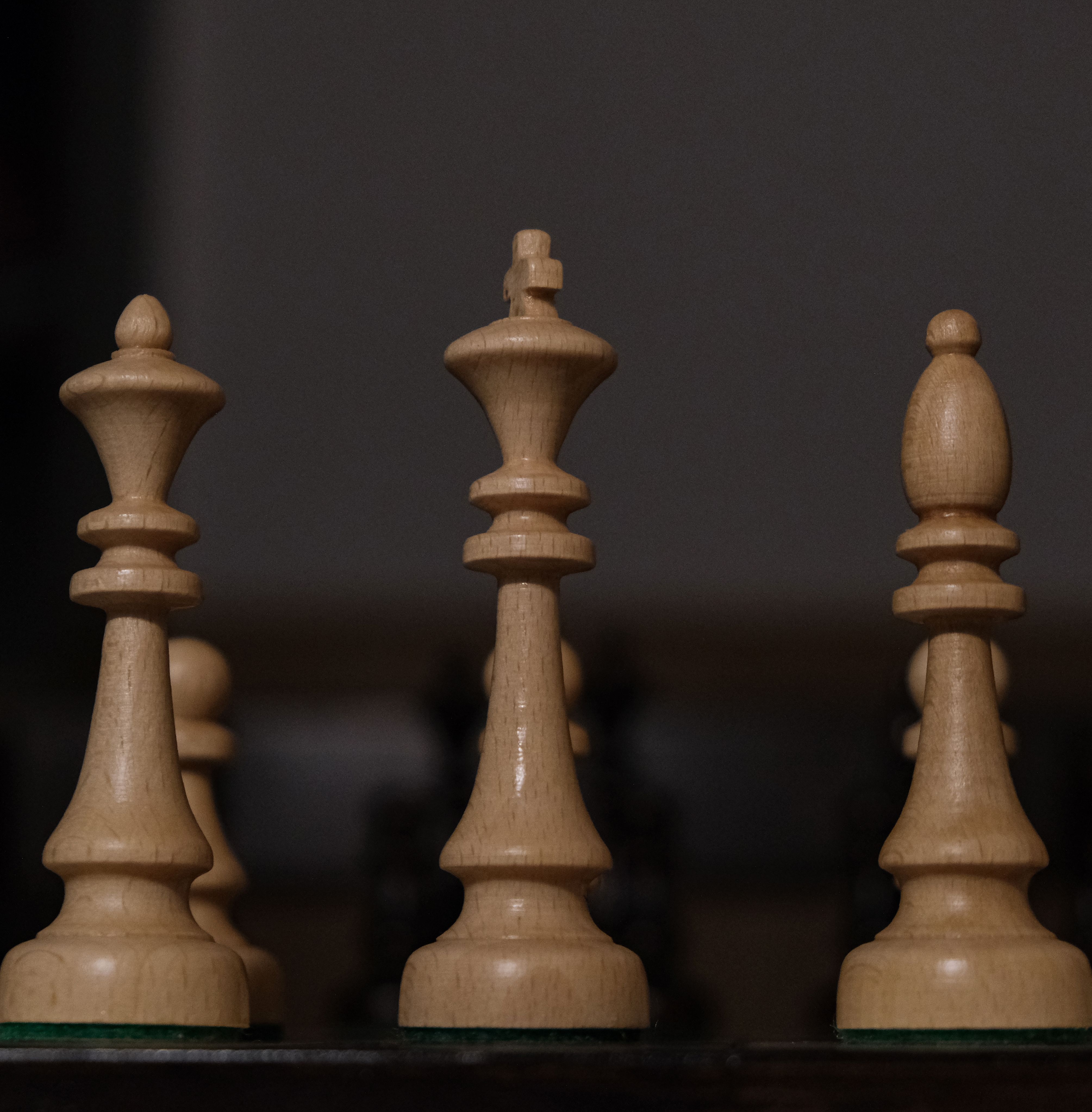 Close-up view of wooden chess pieces on a board showcasing a king, queen, and bishop.