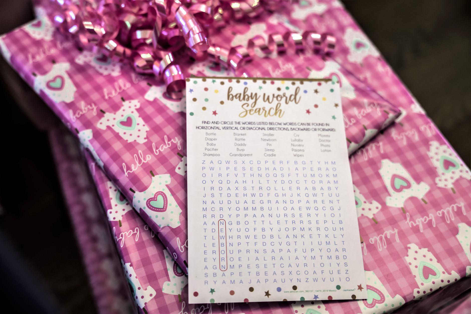 A close-up of a baby shower gift wrapped in pink paper with a word search game.