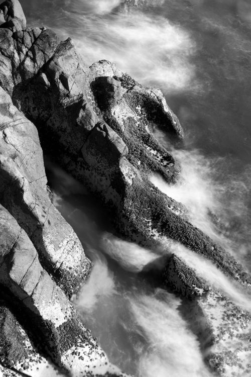 Free Black and white photograph of a rugged coastline with swirling waves, showcasing dramatic textures. Stock Photo