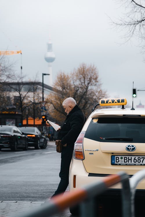 A man reading a newspaper while standing next to a taxi