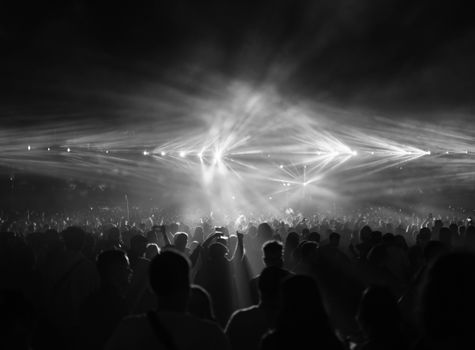 A dramatic black and white photo capturing a crowd at a night concert with bright stage lights.