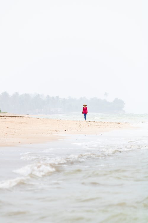 Photo of a Woman Walking on a Beach in the Distance 