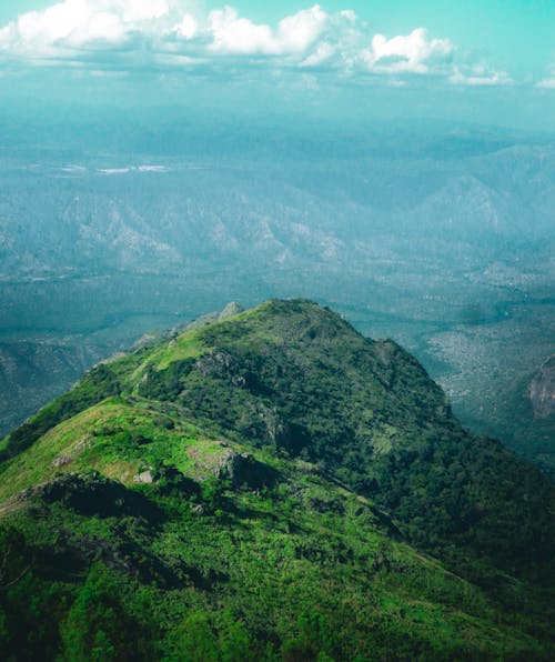 A view of a green mountain with clouds in the sky