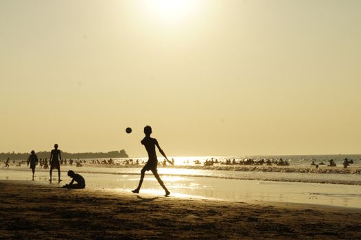 Silhouette of children playing on a crowded beach with the sun setting over the ocean.