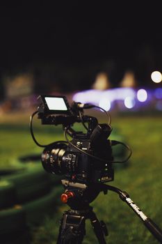 A professional video camera mounted on a tripod set up outdoors at night.
