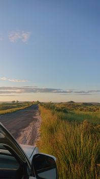 Tranquil road in the countryside with grassy fields and a clear sky at sunset.