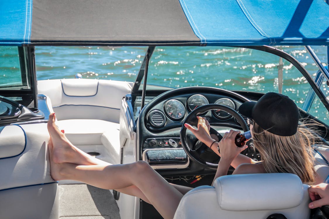 Free Woman Wearing Black Cap Holding Bottle on White Speedboat during Daytime Stock Photo