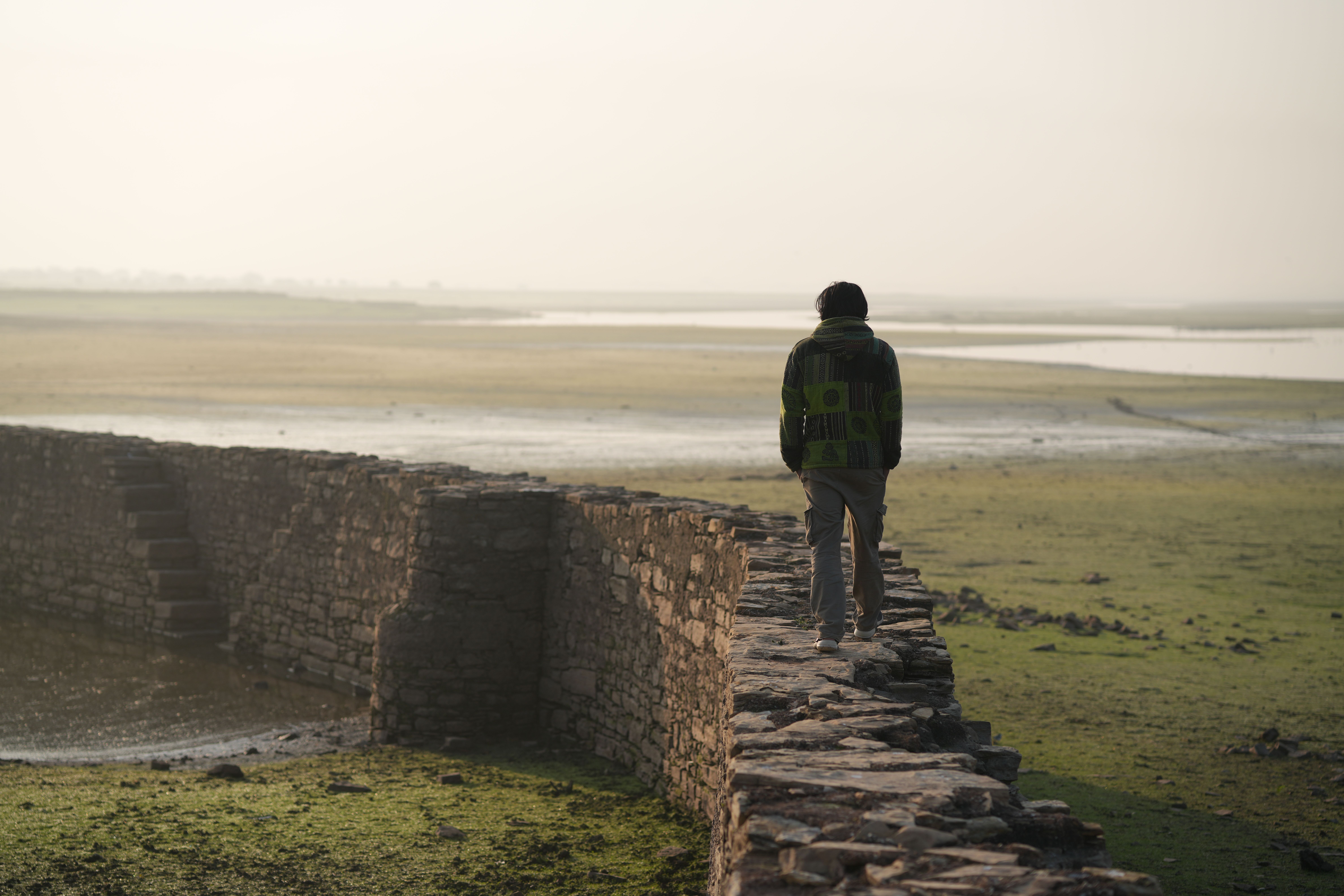 A walker on a dry-stone wall in the open British countryside — classic Barbour territory.