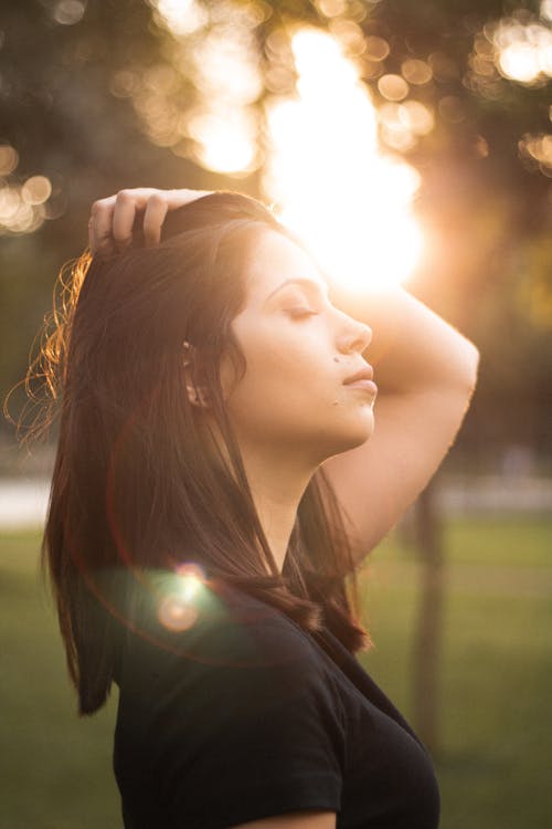 Zijaanzichtfoto Van Een Vrouw Met Haar Ogen Dicht En Houdt Haar Haar Vast Terwijl Het Zonlicht Op Haar Gezicht Schijnt