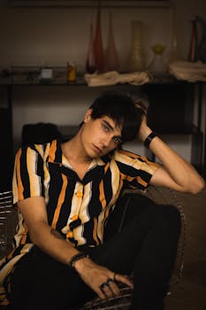 一位穿着条纹衬衫的时尚年轻人若有所思地坐在室内