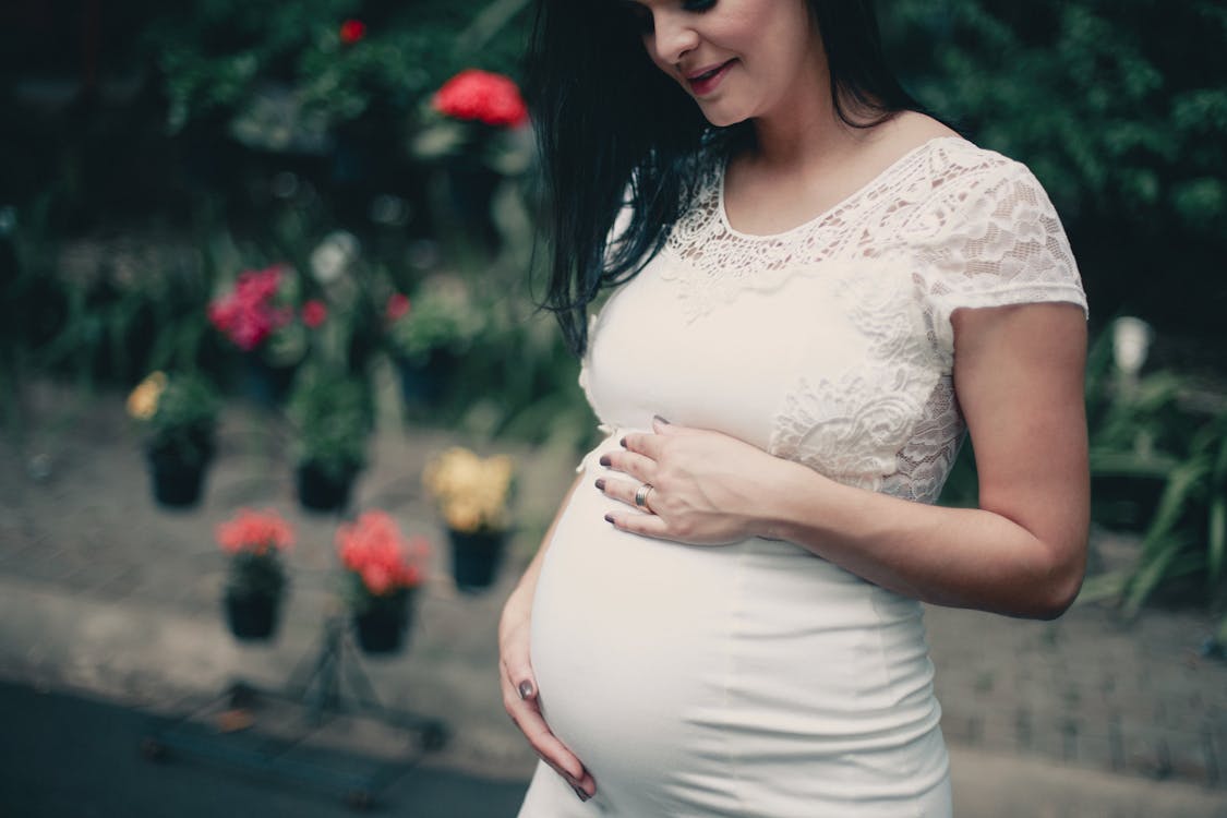 Free Close-up Photo of Pregnant Woman In White Dress Holding Her Stomach Stock Photo