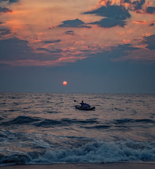 Free A man in a kayak paddling in the ocean at sunset Stock Photo