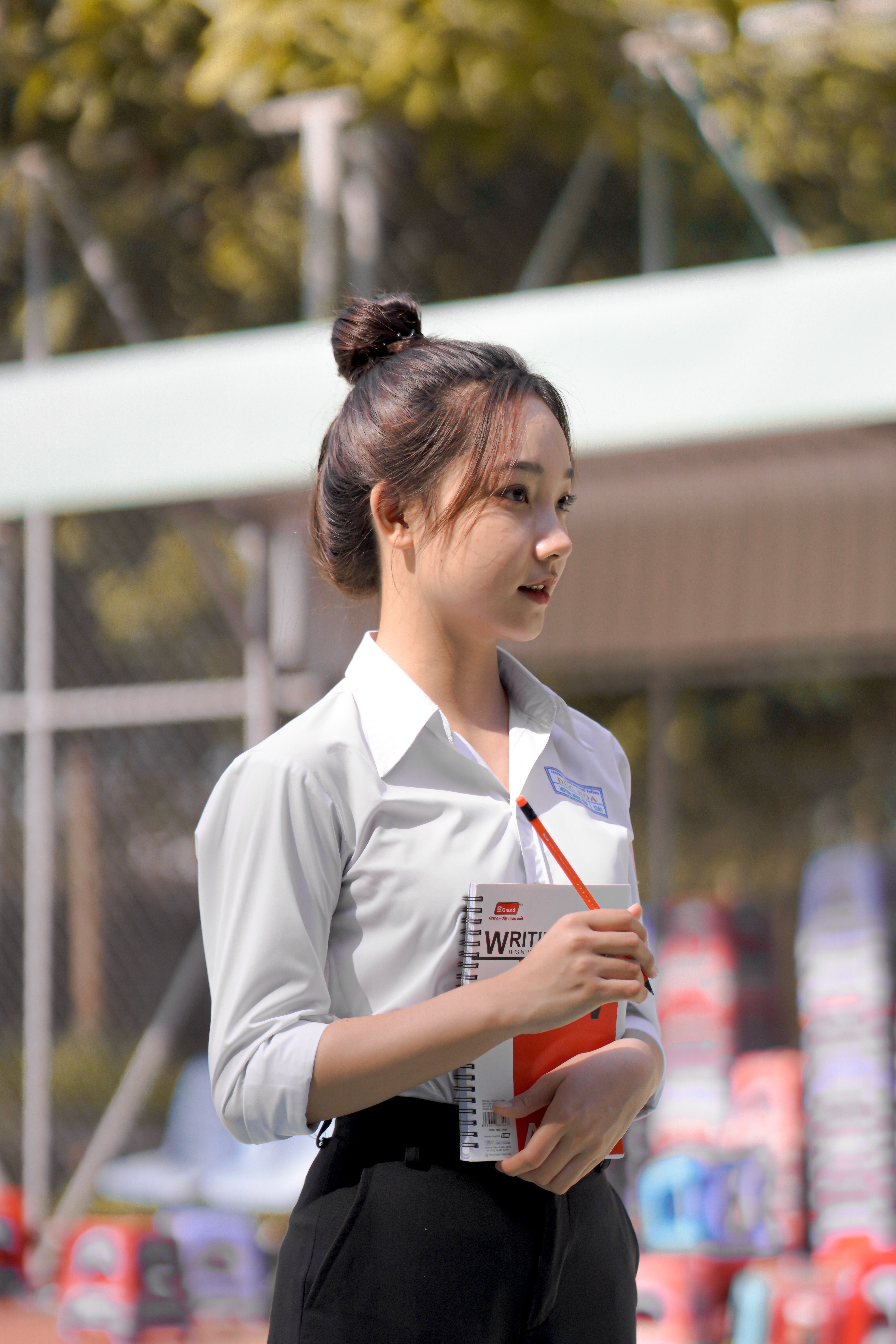 Young Asian student holding notebook outdoors in school uniform on a sunny day.
