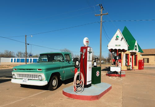 無料 ガソリンポンプステーションの横にある緑色のシングルキャブピックアップトラック 写真素材