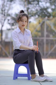Confident young woman wearing a school uniform seated outdoors on a bright day.