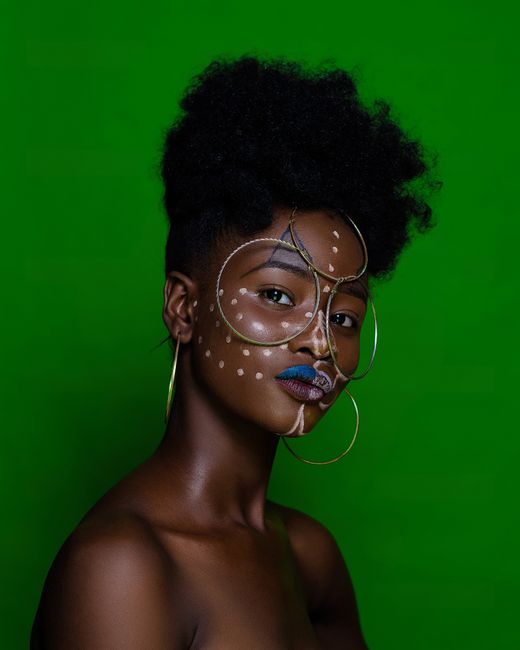 Elegant portrait of a woman with afro hairstyle adorned with creative face paint and jewelry.