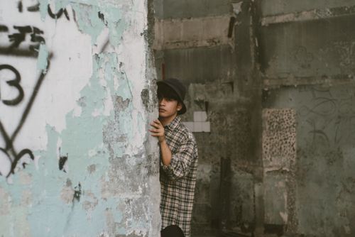 Free Man in checkered shirt hiding behind a weathered, graffitied wall in an abandoned building. Stock Photo