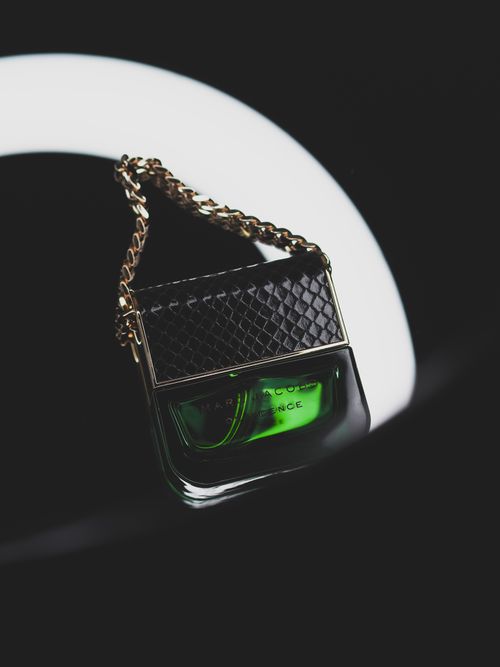 Free Stylish green perfume bottle with chain detail set against a black background. Stock Photo