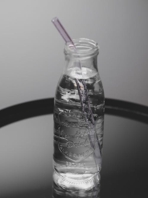 A glass bottle with a straw and a water bottle