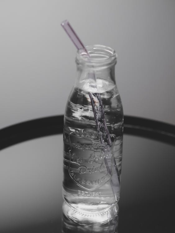 A glass bottle with a straw and a water bottle