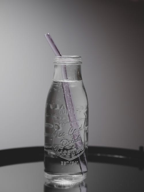 A glass bottle with a straw and a purple straw
