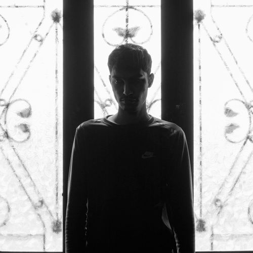 Free Silhouette of a man standing by a decorative window, captured in black and white for a moody effect. Stock Photo