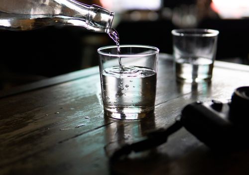Free A clear glass of water being poured from a bottle, set on a rustic wooden table in a dimly lit indoor setting. Stock Photo