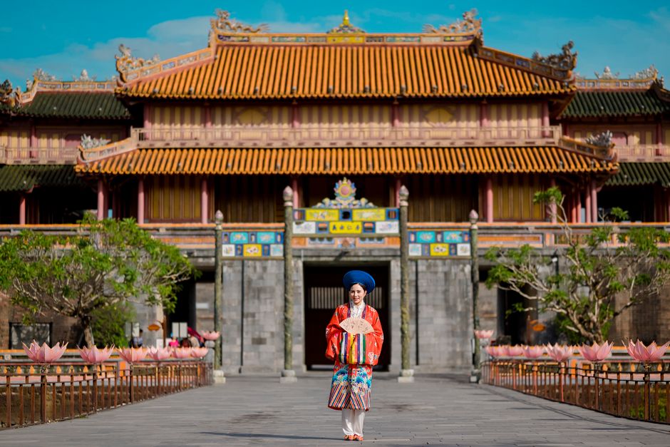 Asian woman in traditional attire stands before Hue Imperial City, Vietnam's historic landmark.