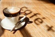 早晨的阳光下，木桌上的一杯温暖卡布奇诺配着拿铁艺术