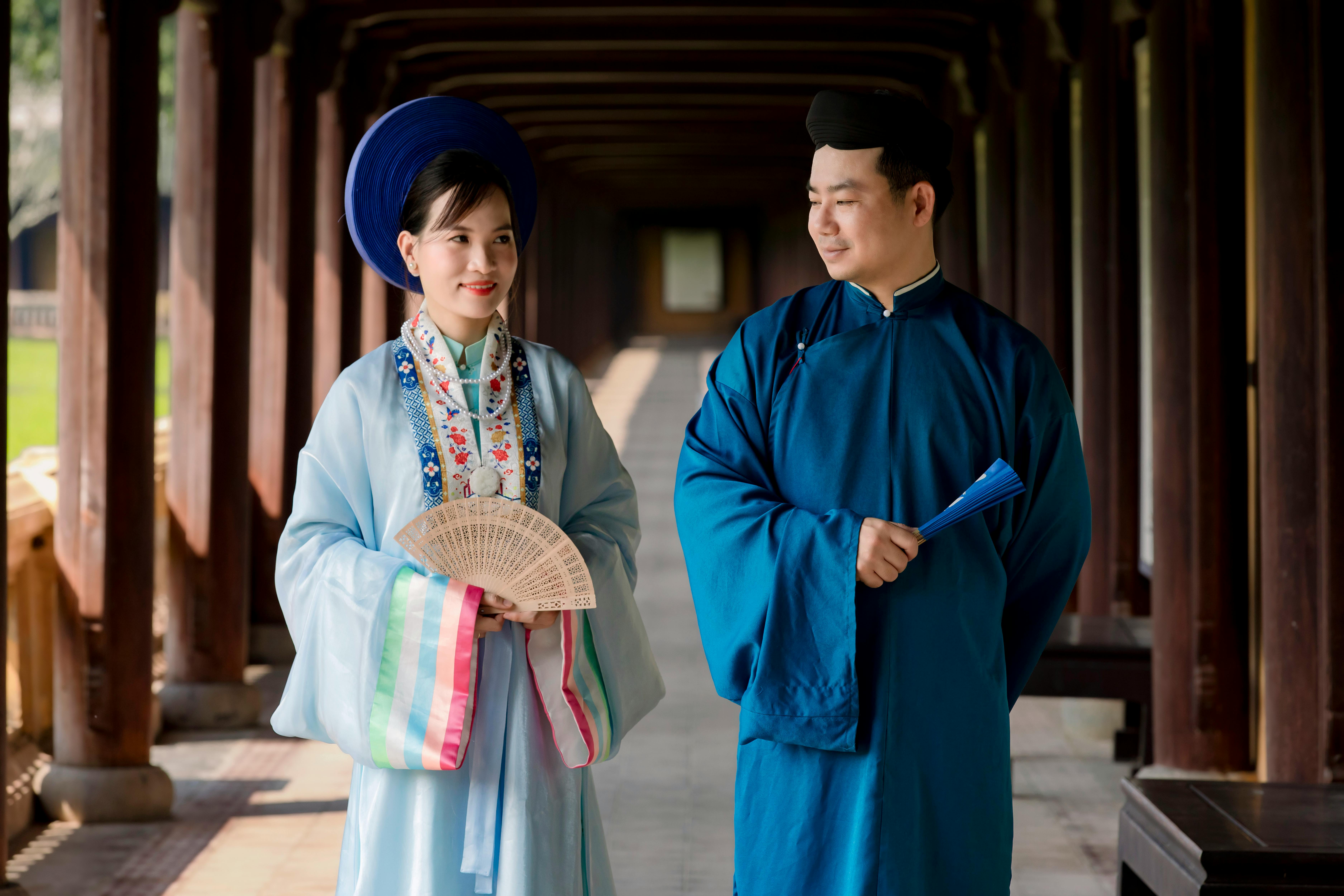 Couple in traditional Vietnamese clothing walking in historical corridor.