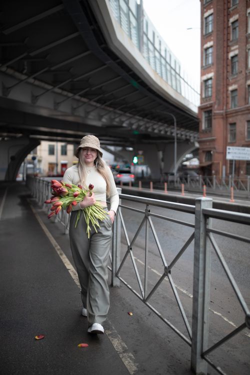 Free A fashionable woman holding tulips walks on an urban street under a bridge. Stock Photo
