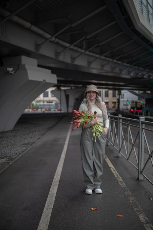 Free A fashionable woman stands under an urban structure holding a bouquet of tulips. Stock Photo